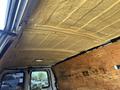 Interior ceiling of a 2012 Chevrolet Express van with yellow insulation and a wooden panel on the side