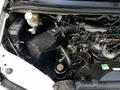 A close-up view of the engine compartment of a 2003 Mitsubishi Delica showing various engine components including the battery and air intake system