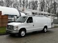 A white 2009 Ford Econoline van with a raised bucket lift mounted on top parked beside a fence