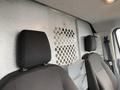 The interior of a 2018 Ford Transit showing two black fabric front seats and a metal partition with circular cutouts separating the driver area from the cargo area