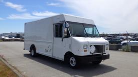 A white 2011 Ford Econoline delivery truck with a boxy shape and large front windows is parked on a paved surface