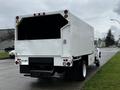 A white 2013 Ford F-650 truck with a boxy cargo area and a simple rear design backed onto a street