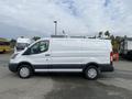 A white 2017 Ford Transit van with a sliding side door and black trim is parked, showcasing a spacious cargo area and modern design features