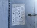 A weathered safety information sign on a metal door outlining various hazards such as electrocution and explosion risks associated with equipment operation