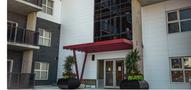 Two-bedroom two-bathroom sublet entrance featuring a modern design with a red canopy and large glass doors flanked by potted plants