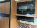A black microwave mounted above a kitchen counter in a recreational vehicle with digital controls and a clock display