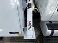 A white 2011 International 4300 truck with a visible hydraulic arm mechanism and caution warning labels on the side