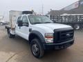 A 2009 Ford F-450 SD with a flatbed design featuring a white exterior and black front grille positioned at an angle with visible amber warning lights