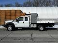 A white 2011 Ford F-450 SD with a flatbed and utility boxes on the back is parked on the street