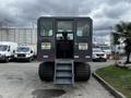 A 2023 Prinoth Panther T6 wheeled vehicle features a cab with large windows and steps at the rear for access with caution signs displayed about headroom and steps