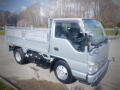 A silver 2008 Isuzu Elf with a flatbed design and two doors is parked, showcasing its compact truck features and chrome side mirrors