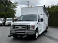 A white 2013 Ford Econoline van with a utility box on the back and a black grille mounted with ladder racks