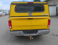 A yellow 2015 RAM 1500 pickup truck with a cap on the bed and a chrome rear bumper featuring a tow hitch