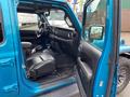 Interior of a blue 2020 Jeep Wrangler with black leather seats and an open front door showing the dashboard and steering wheel