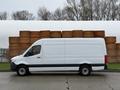 A 2019 Mercedes-Benz Sprinter van in white with a high roof parked alongside stacks of wooden materials.