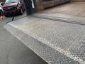 A metallic truck loading ramp with a diamond plate pattern and a slight wear showing signs of use