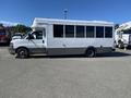 A 2020 Chevrolet Express passenger bus with a white body and gray lower section featuring large windows on the side and a step at the door for entry