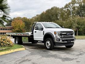 A white 2022 Ford F600 flatbed truck with a cab and a large flatbed cargo area is parked at an angle