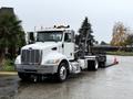 A 2020 Peterbilt 330 truck with a flatbed and a crane mounted on the back parked on a wet surface