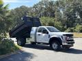 A 2019 Ford F-550 flatbed truck with a black dump bed is parked at an angle with the bed raised