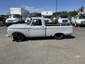 A 1962 Ford F-100 pickup truck in light gray featuring a custom stance and black wheels