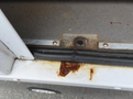 A close-up view of the rusted metal base and rubber trim of a 2020 Chevrolet Express showing signs of corrosion and wear