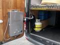 A 2010 Mercedes-Benz Sprinter van with a silver water heater mounted on the rear door and a propane tank visible inside the cargo area