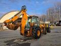 A 2015 Case 590SN backhoe loader with yellow and black coloring features a front bucket and a rear digging arm, parked on a surface with some dirt and tire tracks