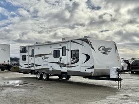 A 2013 Keystone Cougar travel trailer featuring a white exterior with black and gray designs and dual axles