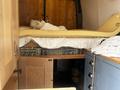 A 2010 Mercedes-Benz Sprinter van interior featuring a bed with a foam mattress and white bedding alongside wooden cabinets and storage compartments