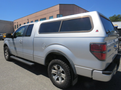 A silver 2014 Ford F-150 pickup truck with a cap on the truck bed and off-road tires is shown from the side