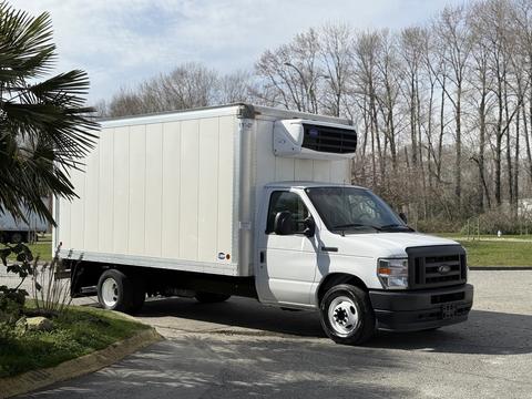 A 2023 Ford E-450 truck with a white box cargo area and a cooling unit mounted on top parked on a driveway