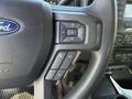 Close-up of a steering wheel in a 2018 Ford F-150 featuring media controls and a Ford logo in the center