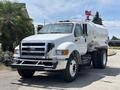 A white 2015 Ford F-750 fuel truck with a large tank in the cargo area and various equipment on top of the cab