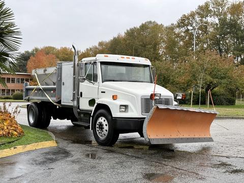 A white 2003 Freightliner FL70 truck with a mounted snow plow and a rear salt spreader attached