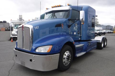 A blue 2015 Kenworth T660 truck with a shiny chrome grille and headlights sits prominently in the foreground