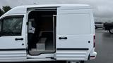 A white 2012 Ford Transit van with the side door open revealing the interior space and seating area