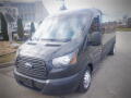 A 2015 Ford Transit van in dark gray parked with a streamlined design featuring a large front grille and simple headlights