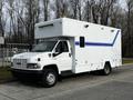 A white 2006 GMC C5000 box truck with blue stripes and a raised roof is parked facing the viewer, featuring a front cab and large cargo area with windows and lights atop