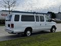 A white 2014 Ford Econoline van parked on the street with a sliding side door and rear windows visible