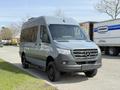 A 2019 Mercedes-Benz Sprinter van in a light gray color with a high roof and large front grille parked on a street