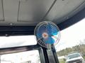A small electric fan with blue blades mounted inside the cabin of a mini excavator