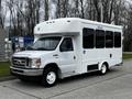 A white 2016 Ford Econoline shuttle bus with large windows and a ramp for accessibility parked on a paved surface