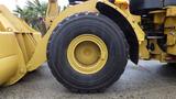 A yellow Caterpillar 972M XE wheel with deep treads and a sturdy rim positioned to the side of a loading bucket