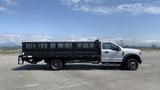 A 2019 Ford F-550 in white and black with a flatbed and metal stake sides parked in an open area