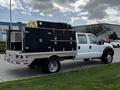 A 2007 Ford F-550 truck with a flatbed and a large black toolbox mounted on the back featuring multiple compartments and reflective safety markings