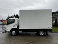 A 2012 Mitsubishi Fuso FE box truck with a white cargo area and a gray cab parked on a wet surface