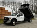 A white 2019 Ford F-550 dump truck with the bed raised showcasing its cargo area