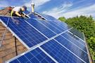 A person installing solar panels on a roof with multiple solar panels extending in the foreground