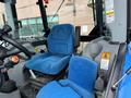 A blue seat in the cab of a 2016 New Holland T475 tractor with controls and safety labels visible